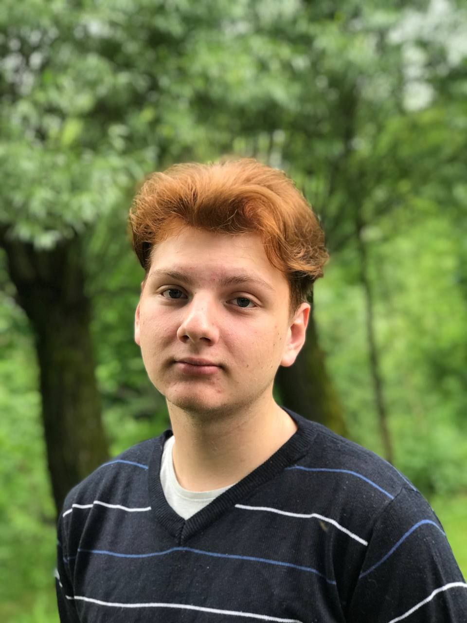 Adam Zieliński with red hair wearing a striped sweater in a green outdoor setting